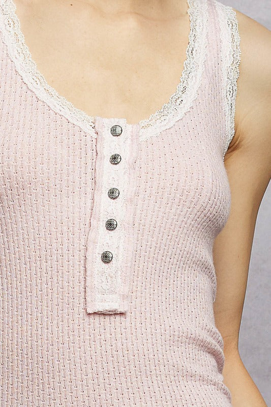 Close-up of a light pink tank top with lace trim and buttons on a neutral background