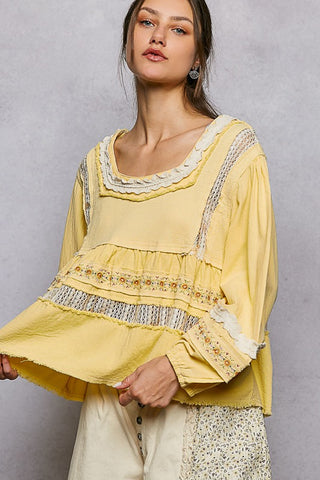 Woman wearing a yellow blouse with lace details against a gray background