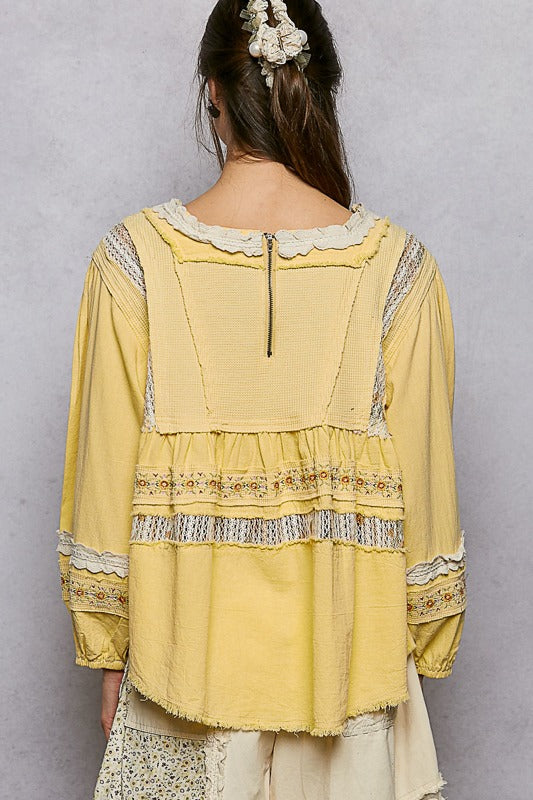 Yellow embroidered blouse with lace details on a gray background