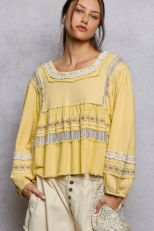 Woman wearing a yellow blouse with lace details against a gray background