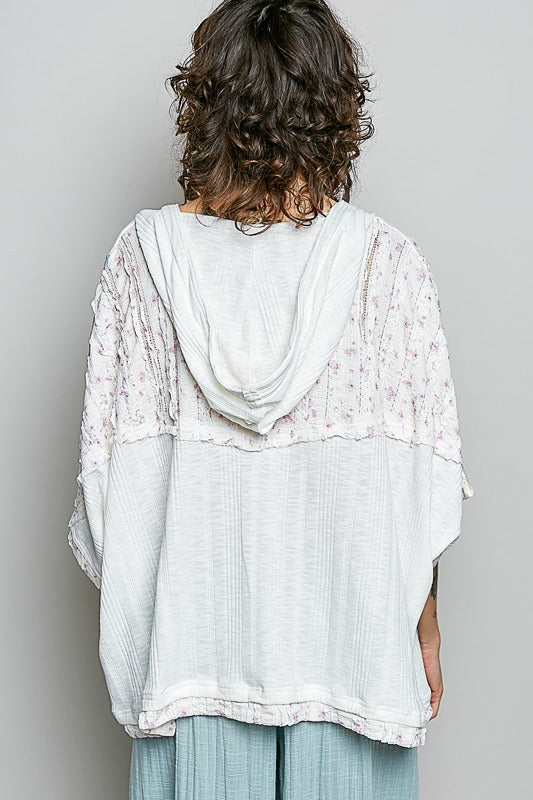 Person wearing a light-colored, textured top with a hood against a plain background