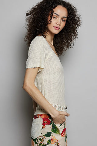 Woman wearing a light-colored top and floral pants against a plain background
