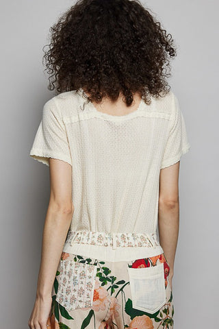 Person wearing a light-colored top and floral pants against a plain background