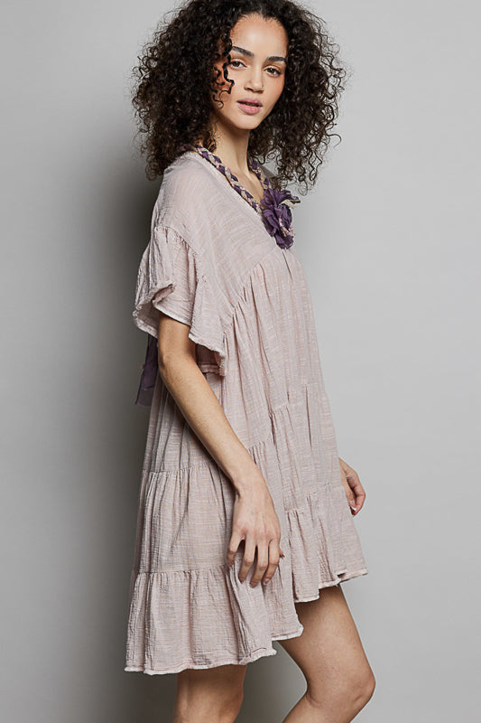 Woman wearing a light-colored dress with a floral accessory against a plain background
