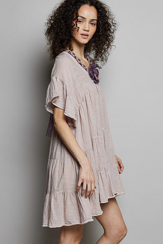 Woman wearing a light-colored dress with a floral accessory against a plain background