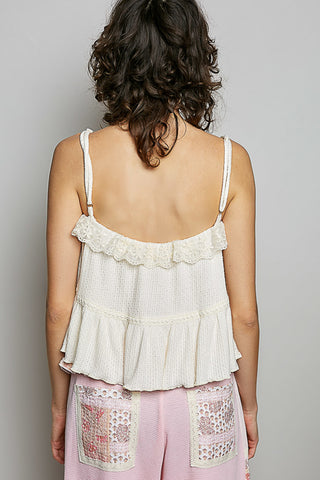Woman wearing a white lace top and pink pants with lace details on a plain background