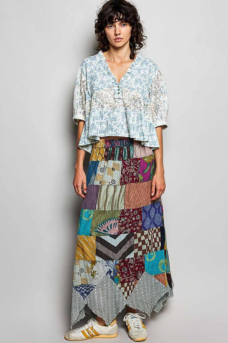 Woman wearing a patterned top and colorful patchwork skirt on a plain background