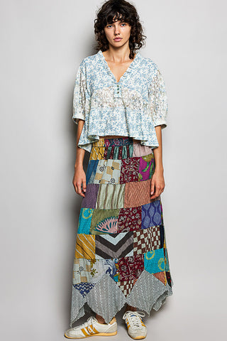 Woman wearing a patterned top and colorful patchwork skirt on a plain background