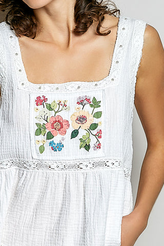 A women wearing a white tank top with a floral patch on it.