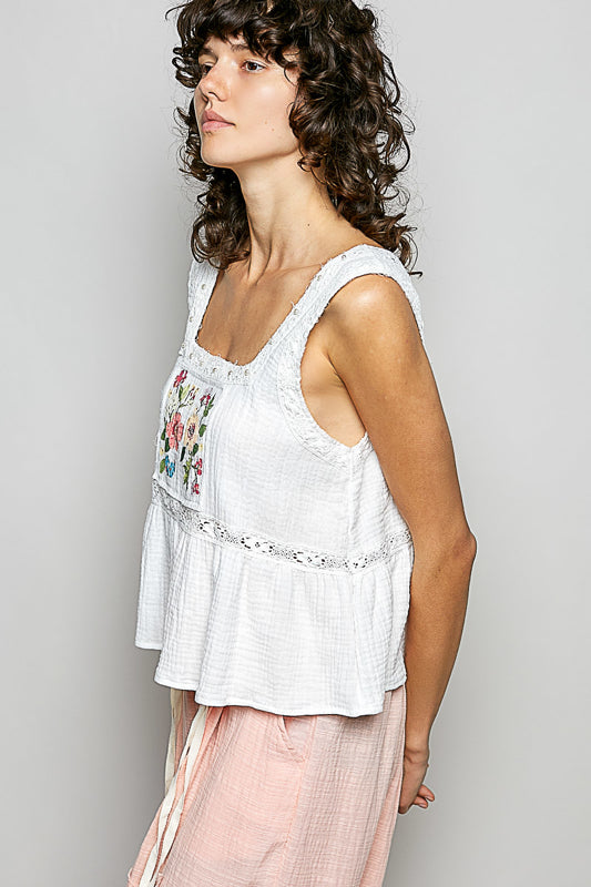 A women wearing a white tank top with a floral patch on it.