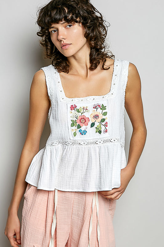 A women wearing a white tank top with a floral patch on it.