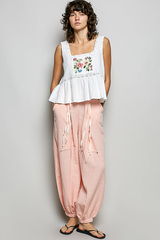 A women wearing a white tank top with a floral patch on it.