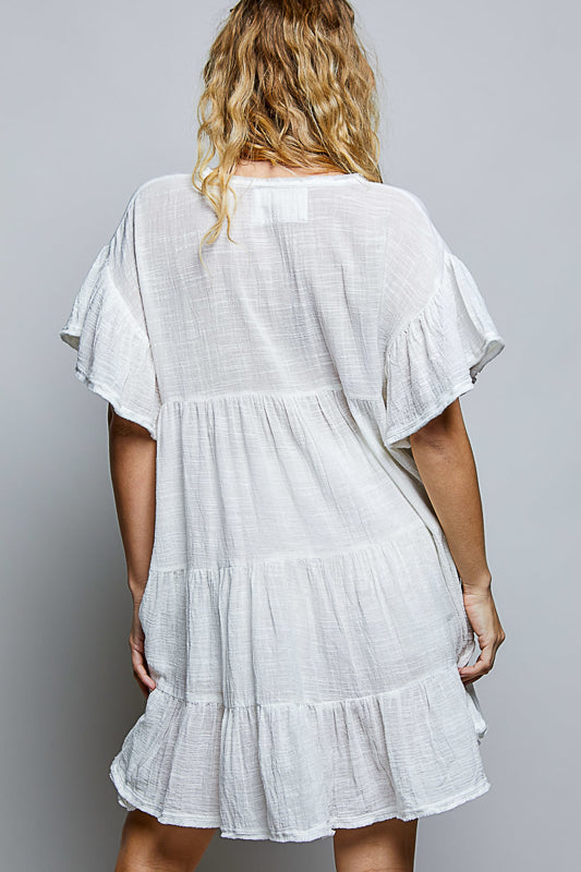 White dress with ruffled layers worn by a person on a gray background