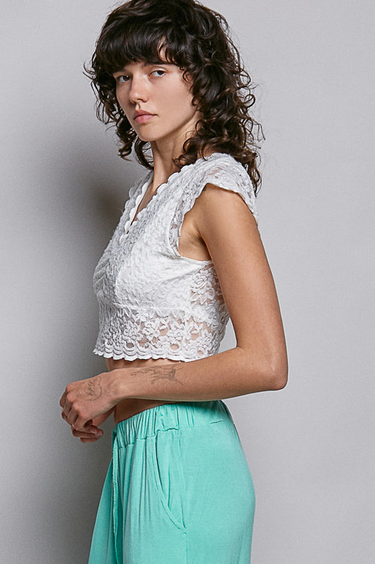 Women wearing a white lace crop top on a plain background. 