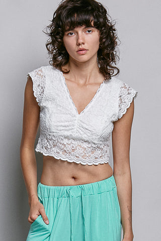 Women wearing a white lace crop top on a plain background. 