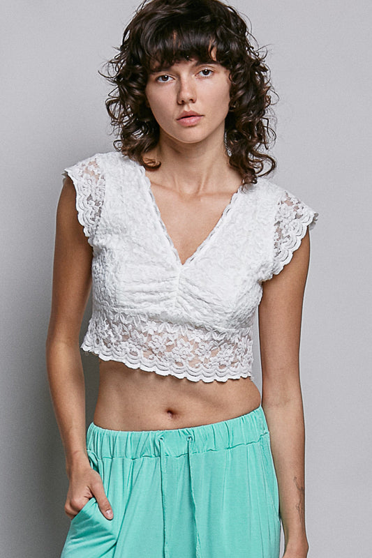 Women wearing a white lace crop top on a plain background. 