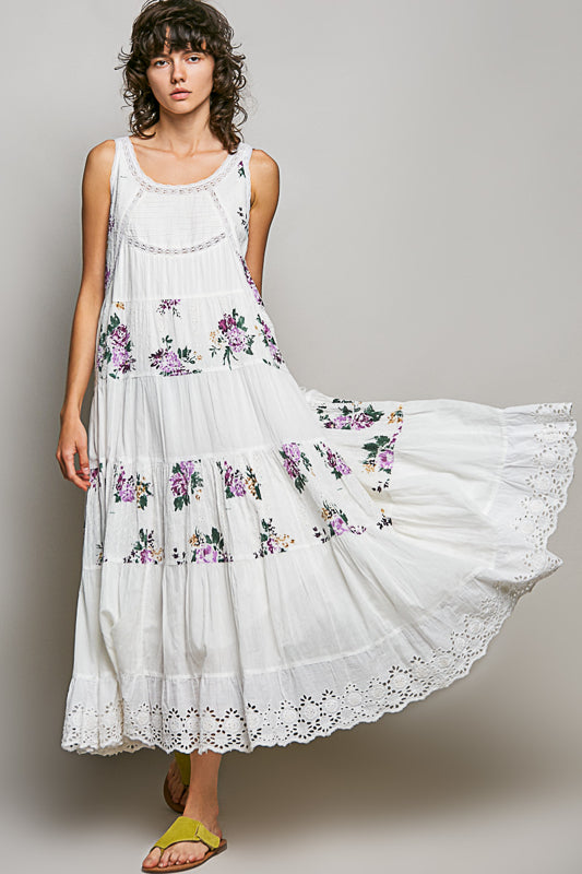 Woman wearing a white dress with floral embroidery on a plain background