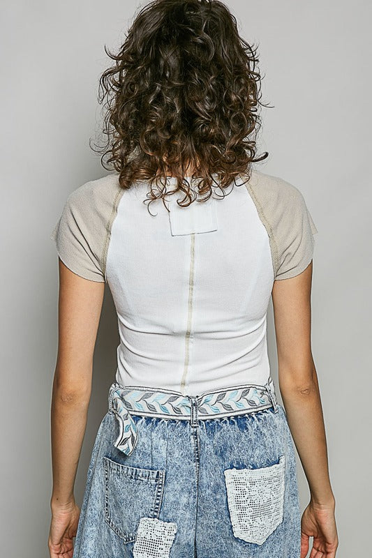 Person wearing a white and beige raglan shirt with a denim skirt on a plain background