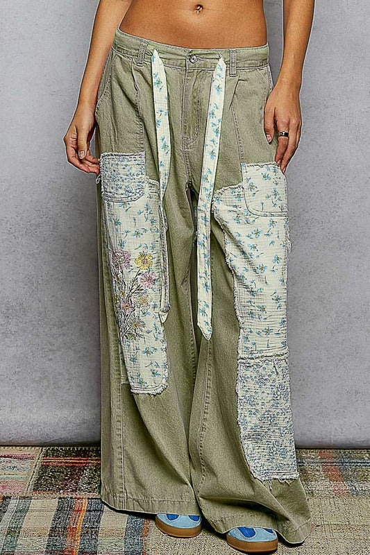 Person wearing a pair of wide-leg pants with floral patchwork on a gray background