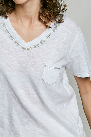 Close-up of a person wearing a light gray t-shirt with decorative trim on a plain background