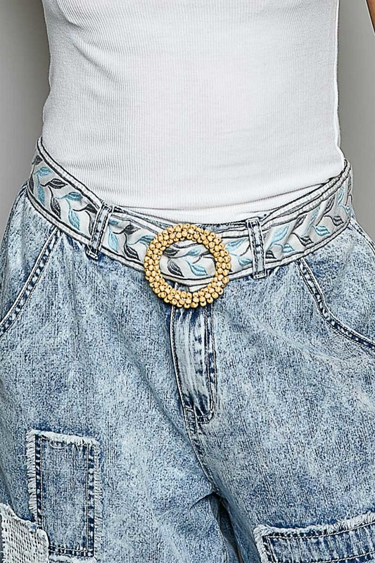Close-up of a person wearing light blue jeans with a decorative belt featuring a gold buckle.