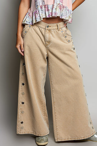 Person wearing beige wide-leg pants with button details on a plain background