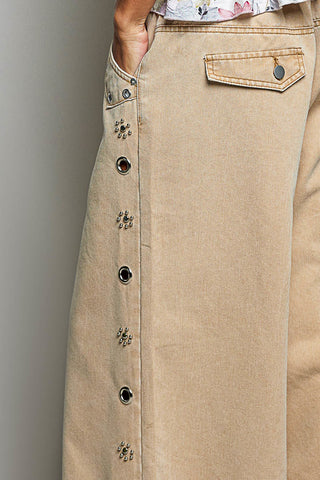 Close-up of a beige skirt with decorative dark buttons down the front, a side pocket with a button flap, and a hand tucked into a side pocket.