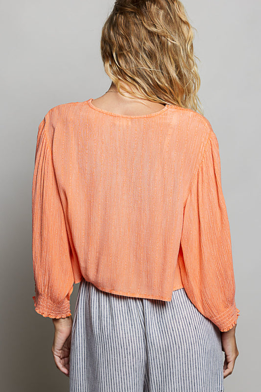 Woman wearing a peach-colored blouse with long sleeves and a gray background