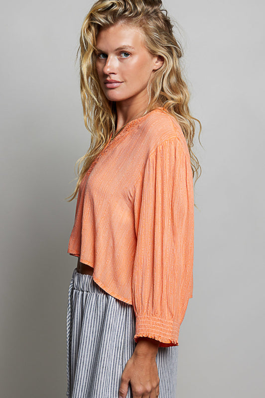 Woman wearing an orange blouse with long sleeves against a gray background