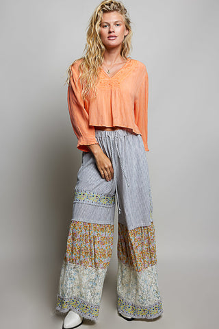Woman wearing an orange top and patterned pants on a gray background