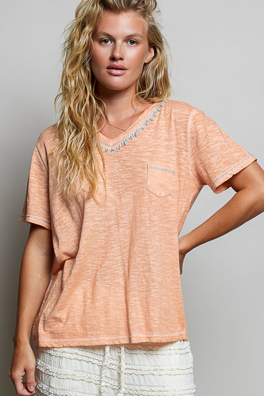 Woman wearing a peach-colored t-shirt with a pocket on a gray background