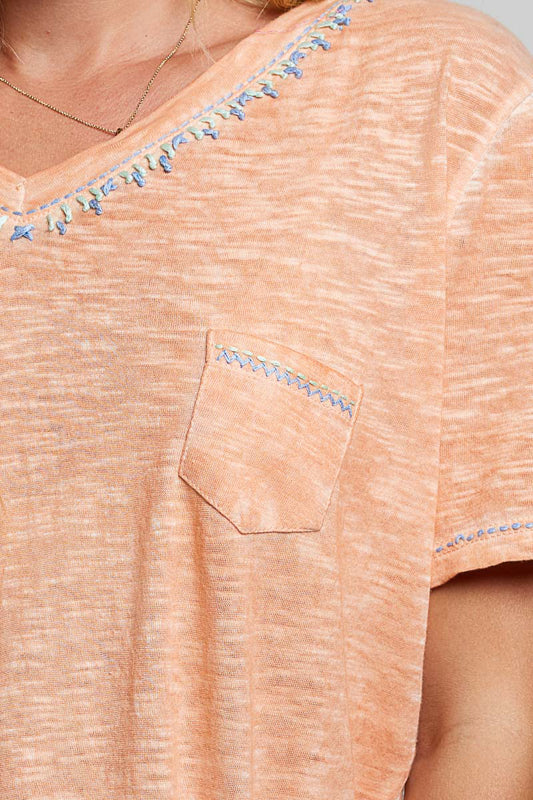 Close-up of a peach-colored shirt with decorative blue beads on a plain background