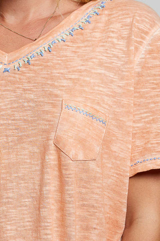 Close-up of a peach-colored shirt with decorative blue beads on a plain background