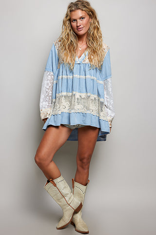 A women wearing a blue lace top against a neutral background.