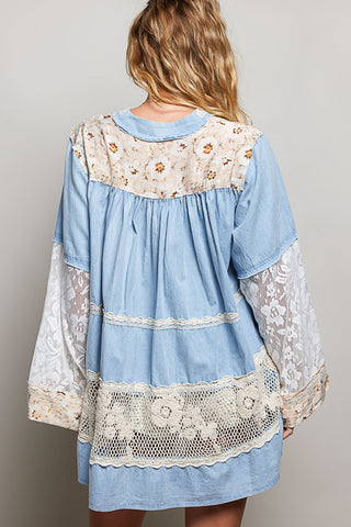 A women wearing a blue lace top against a neutral background.