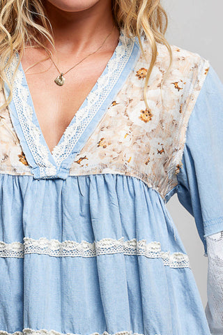 A women wearing a blue lace top against a neutral background.