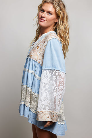 A women wearing a blue lace top against a neutral background.