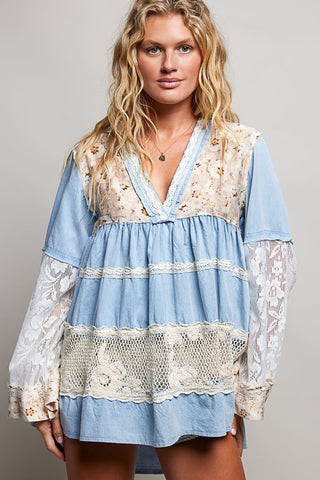 A women wearing a blue lace top against a neutral background.