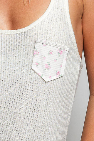 White sleeveless top with floral pocket on a plain background
