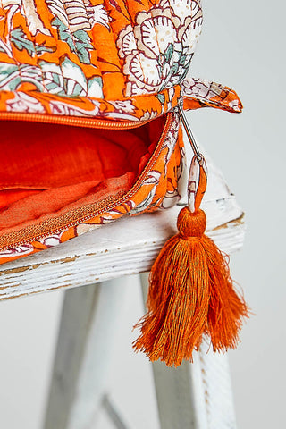 an orange cosmetic case on a stool agaisnt a nuetral background. 