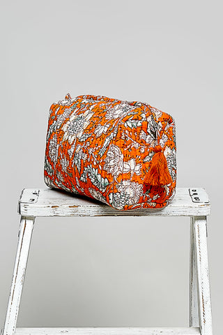 an orange cosmetic case on a stool agaisnt a nuetral background. 