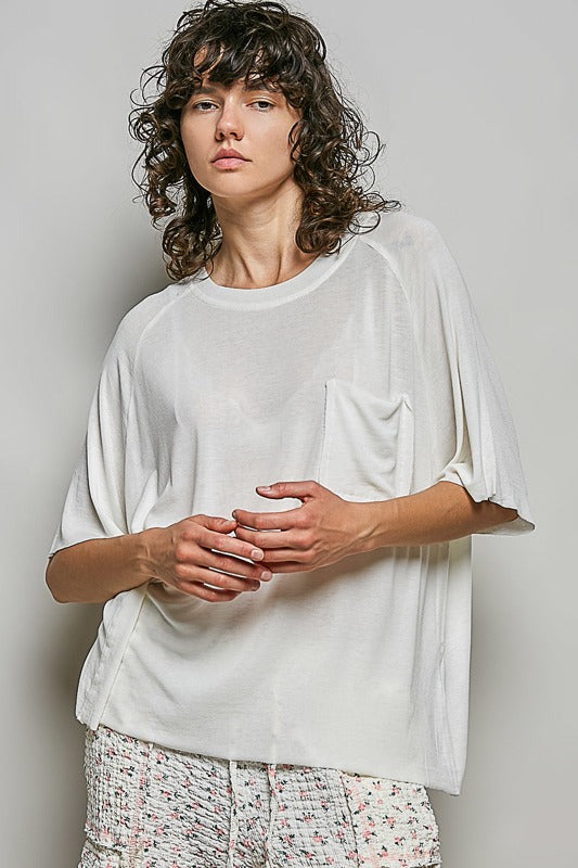 Person wearing a white oversized shirt with floral pants against a plain background