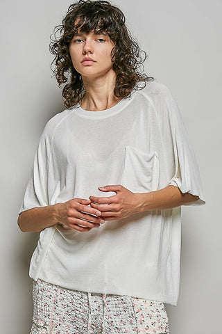 Person wearing a white oversized shirt with floral pants against a plain background