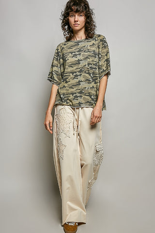 Person wearing a camouflage top and beige pants against a plain background