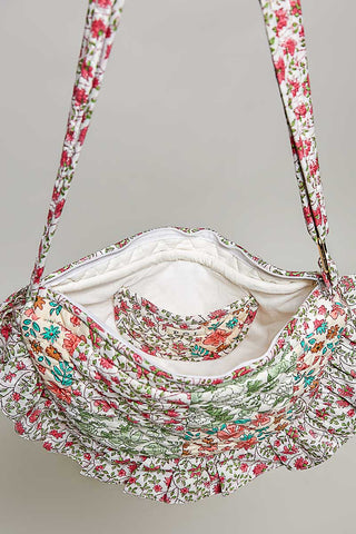 A ruffled shoulder bag with a dense floral print in red, green, and orange on a white background, featuring a white quilted interior lining.