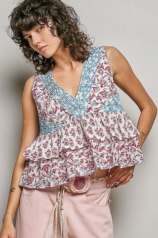A women wearing a pink and blue floral top against a neutral background.