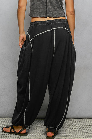 Black harem-style pants with white contrast stitching, shown on a model from the back against a gray wall.