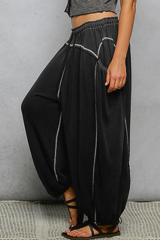 Black harem pants with white piping worn by a person against a gray background