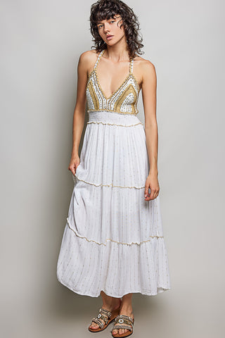 Woman wearing a white and gold dress against a plain background