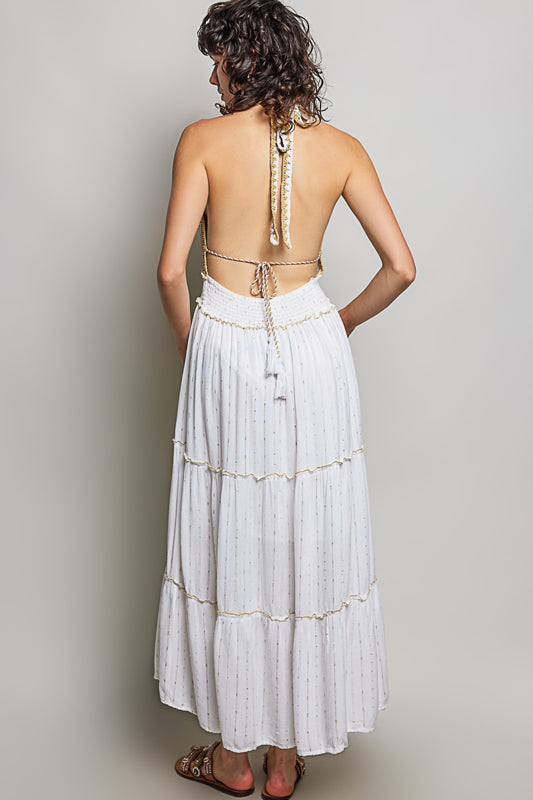 Woman wearing a white dress with gold embellishments against a plain background